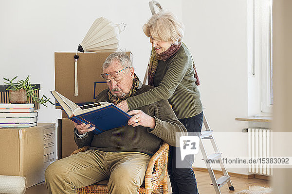 Älteres Ehepaar betrachtet Fotoalbum umgeben von Pappkartons in einem leeren Raum