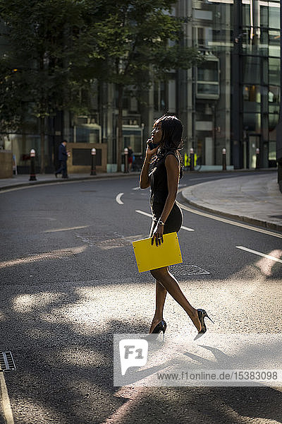 Geschäftsfrau überquert Straße und benutzt Smartphone in der Stadt