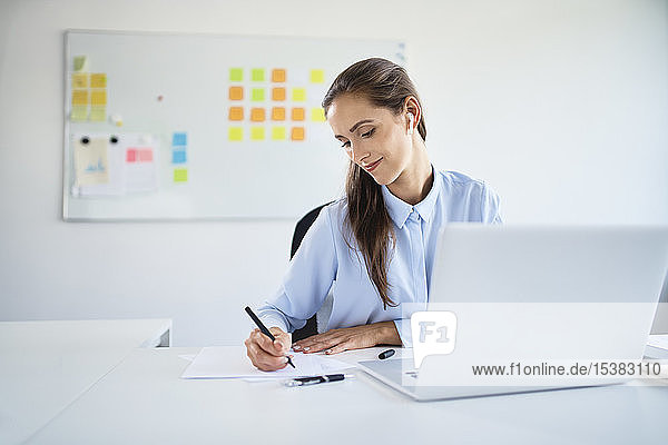 Junge Geschäftsfrau bereitet Geschäftsdokumente vor  während sie im Büro mit dem Laptop arbeitet
