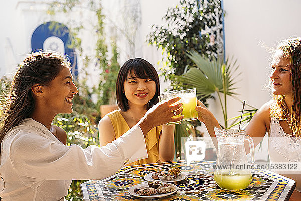 Drei glückliche Freundinnen treffen sich in einem Café mit klirrenden Limonadengläsern