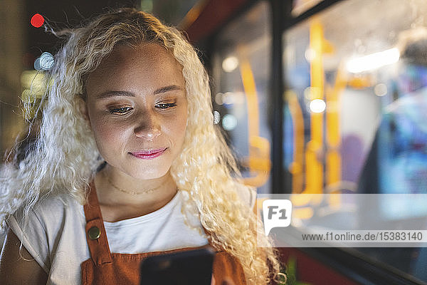 Young woman in London at night looking at her smartphone  bus in the background