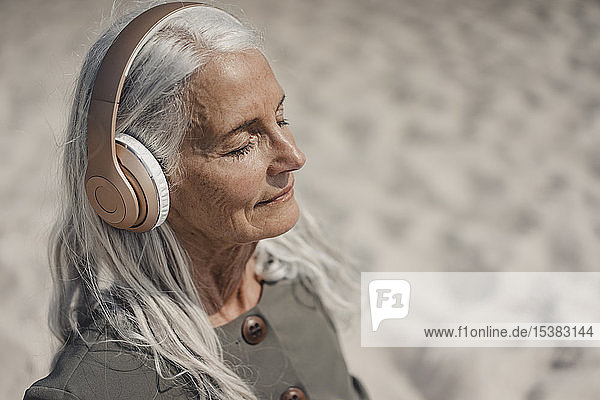 Ältere Frau  die am Strand mit Kopfhörern Musik hört