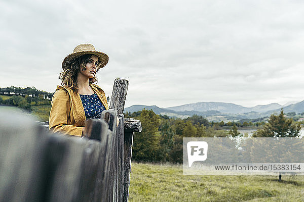 Young curly haired woman wearing a hat  yellow coat and blue t-shirt looking the mountain landscape