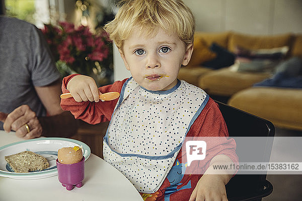 Portrait of blond little boy eating breakfast egg