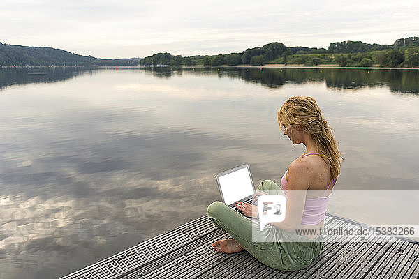 Junge Frau mit Laptop auf einem Steg an einem See