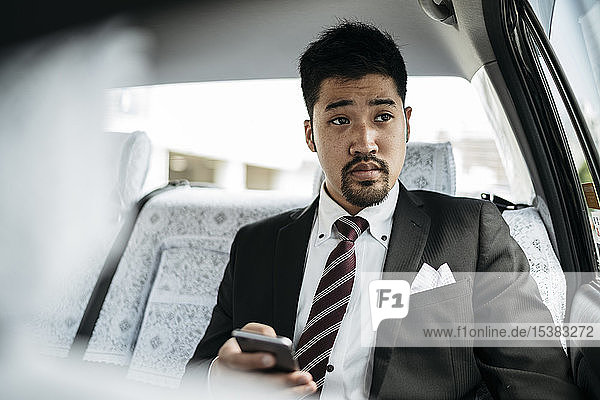 Junger Geschäftsmann mit Handy in einem Taxi