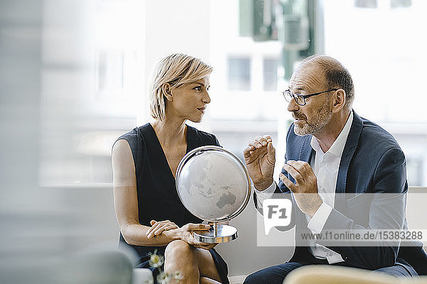 Geschäftsmann und -frau sitzen im Café  schauen auf den Globus und diskutieren über Geschäfte