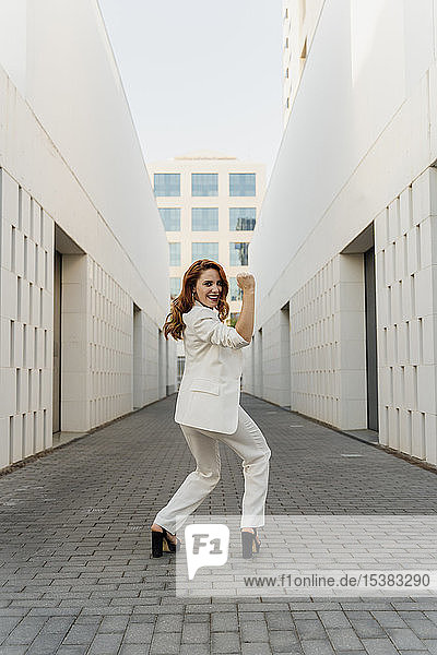 Energische Geschäftsfrau im weißen Hosenanzug  die ihre Muskeln spielen lässt
