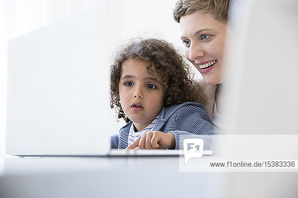 Lächelnde Mutter und Sohn benutzen Laptop zu Hause