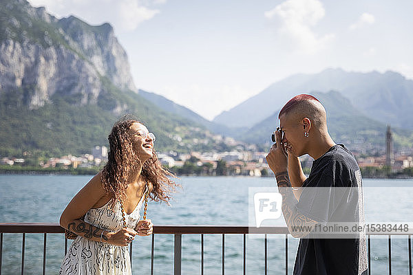 Young man taking photo of his girlfriend in front of Lake Como  Lecco  Italy