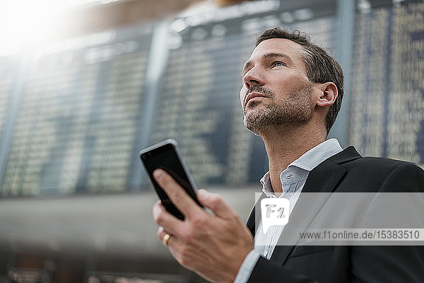 Porträt eines Geschäftsmannes mit Handy bei der Ankunft Abflugtafel am Flughafen