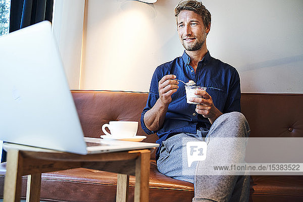 Young businessman eating and using laptop in a cafe