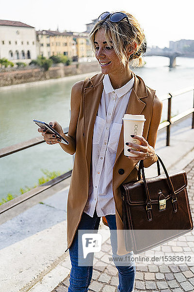 Lächelnde Frau mit Kaffee zum Mitnehmen mit Smartphone in der Stadt