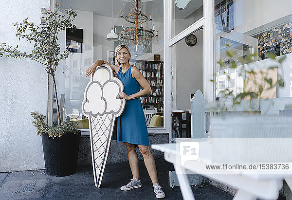 Frau steht vor ihrem Café und hält Eisschild