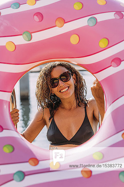 Porträt einer glücklichen jungen Frau hinter einem aufblasbaren Schwimmer in Donutform