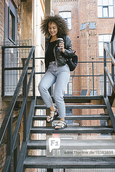 Porträt einer lächelnden Teenagerin mit Kaffee  die die Treppe hinuntergeht