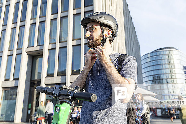 Mann mit E-Scooter in Berlin  Befestigung eines Schutzhelms  Deutschland