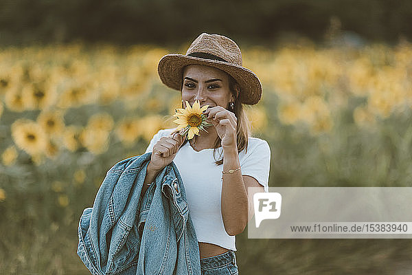 Portrait of young woman with blue denim jacket and hat in a field of sunflowers