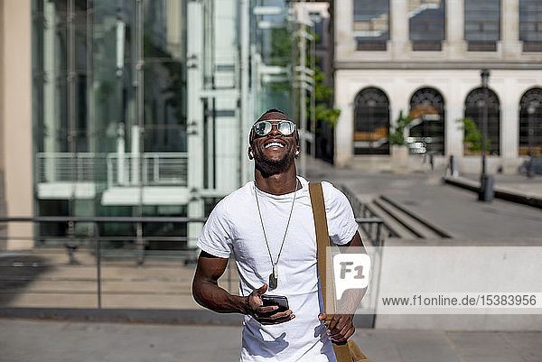 Lächelnder junger Mann benutzt Smartphone und Kopfhörer