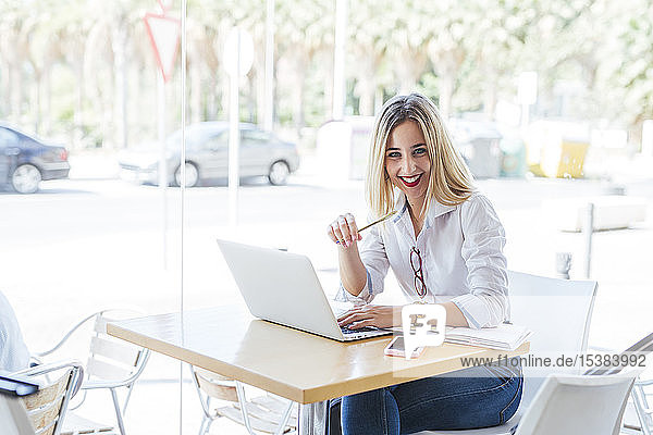 Porträt einer lächelnden jungen Frau mit Laptop auf einem Tisch in einem Cafe