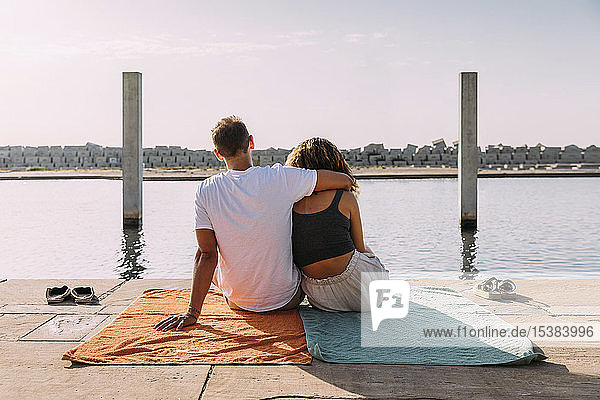 Rear view of young couple sitting on a pier at the sea