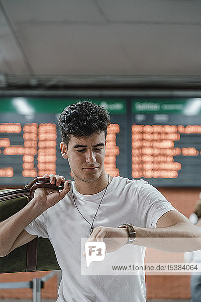 Junger Mann überprüft die Uhrzeit am Bahnhof