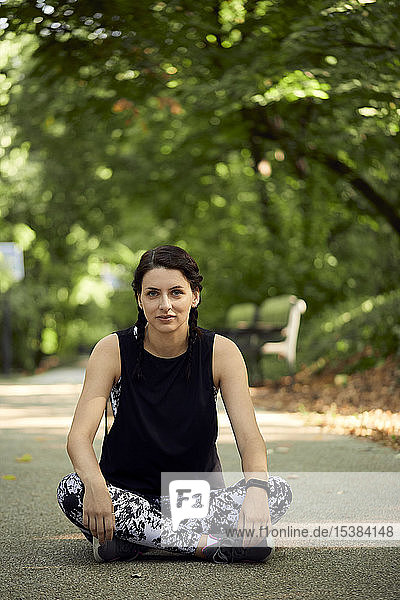 Porträt einer sportlichen jungen Frau am Waldweg sitzend