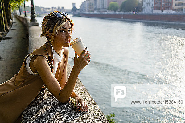 Frau trinkt Kaffee am Flussufer in der Stadt