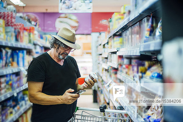 Älterer Mann kauft mit seinem Smartphone in einem Supermarkt ein