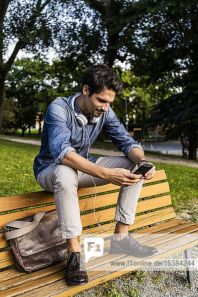 Smiling man sitting on a park bench using his smartphone