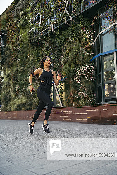 Seitenansicht einer jungen Joggerin beim Laufen in einer Stadt mit einem Gebäude mit Gartenfassade im Hintergrund
