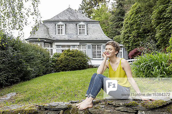 Entspannte Frau sitzt auf einer Mauer im Garten