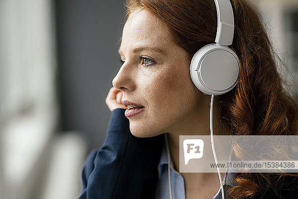 Portrait of redheaded businesswoman listening music with white headphones