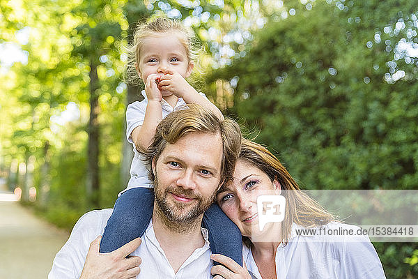 Porträt einer glücklichen Familie in einem Park mit einem Vater  der seine kleine Tochter auf den Schultern trägt