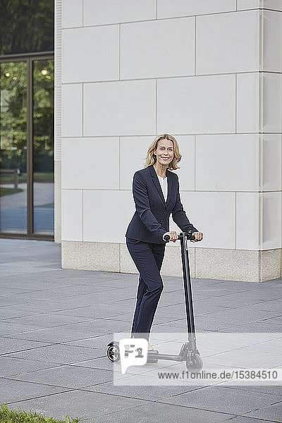 Businesswoman on e-scooter stnading before office building in the city