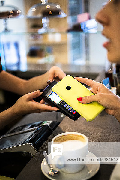 Nahaufnahme eines bargeldlos mit Smartphone zahlenden Kunden in einem Cafe