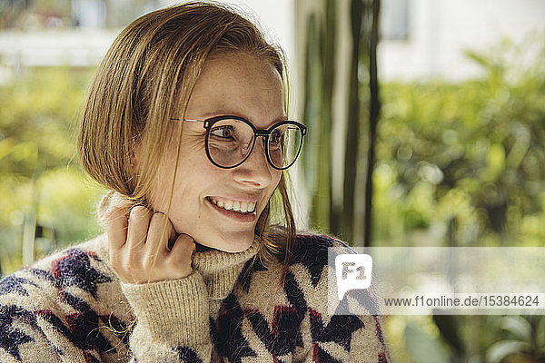 Porträt einer lächelnden jungen Frau mit Brille, die einen flauschigen Pullover trägt und zur Seite schaut