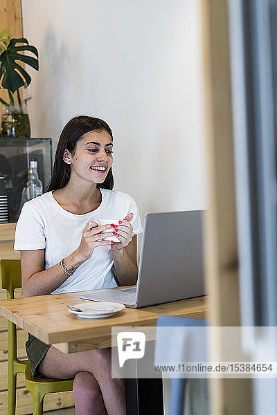 Smiling young woman using laptop in a cafe