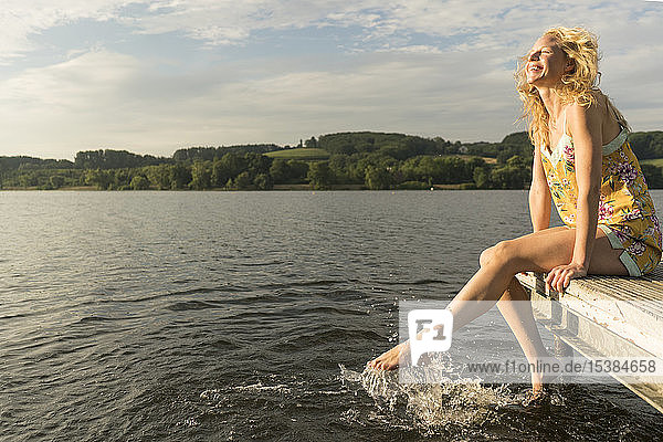Junge Frau sitzt auf einem Steg an einem See mit Füßen im Wasser
