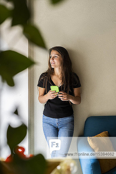 Young woman leaning against a wall holding cell phone