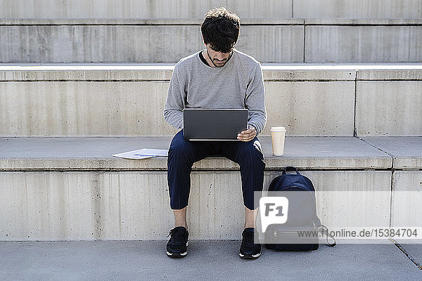Mann sitzt mit Laptop auf einer Außentreppe