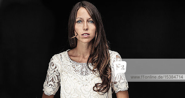 Portrait of young woman with long brown hair against black background