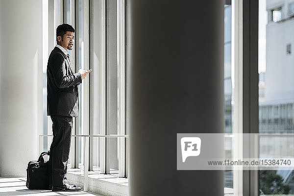 Young businessman with cell phone standing at the window