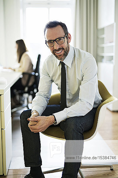 Portrait of smiling businessman in office with employee in background