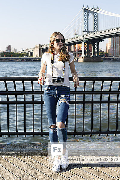 Junge Frau erkundet New York City  steht mit Kamera an der Brooklyn Bridge
