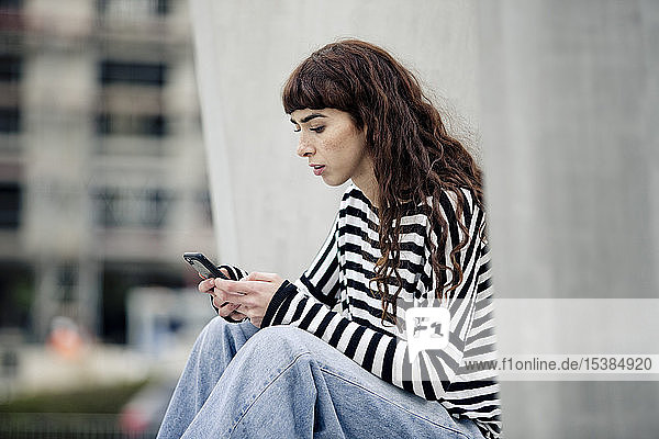 junge Frau  die ein gestreiftes Hemd trägt und ein Smartphone benutzt