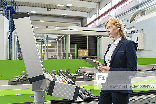Geschäftsfrau benutzt Tablette an Maschine in Fabrik