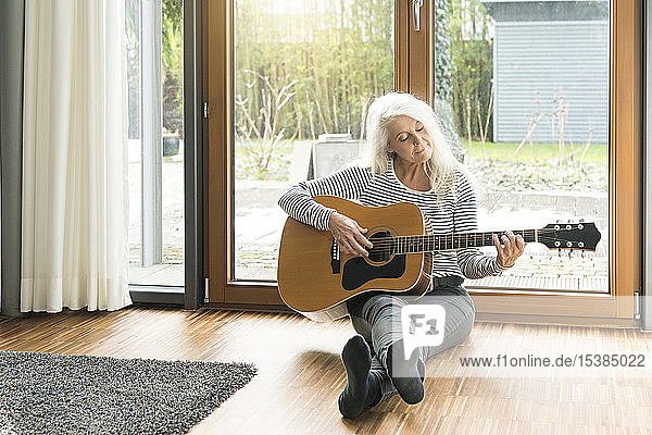 Reife Frau sitzt auf dem Boden im Wohnzimmer und spielt Gitarre