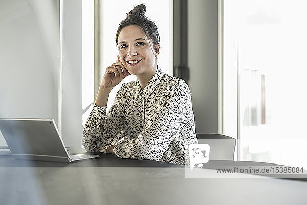 Porträt einer lächelnden Geschäftsfrau mit Laptop  die im Büro am Schreibtisch sitzt