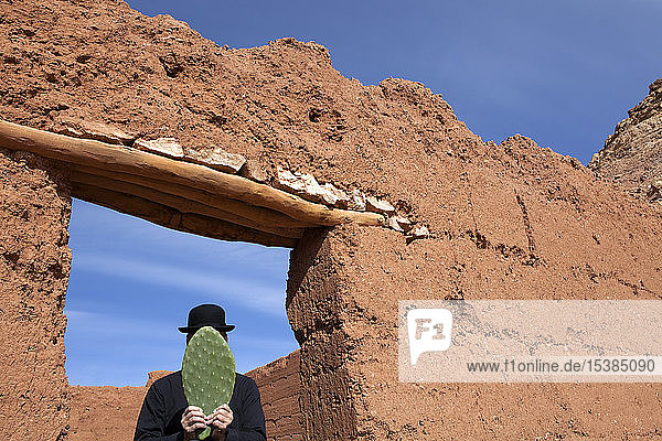 Morocco  Ait-Ben-Haddou  man wearing a bowler hat holding a cactus leaf in front of his face
